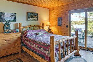 A wooden cabin bedroom with a bed, dresser, lamp, and a painting on the wall. - Upscale Beachfront Log Home on Lake Huron Shores (Drummond)