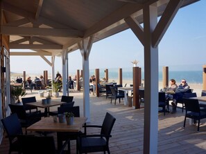 An outdoor café with wooden tables and chairs, overlooking a beach. - Holiday Home in Renesse With Swimming Pool (Renesse)