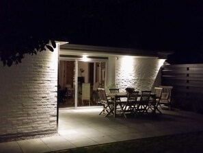 An outdoor patio area with a table and chairs, a glass door entrance, and a brick wall. - Holiday Home in Renesse With Swimming Pool (Renesse)
