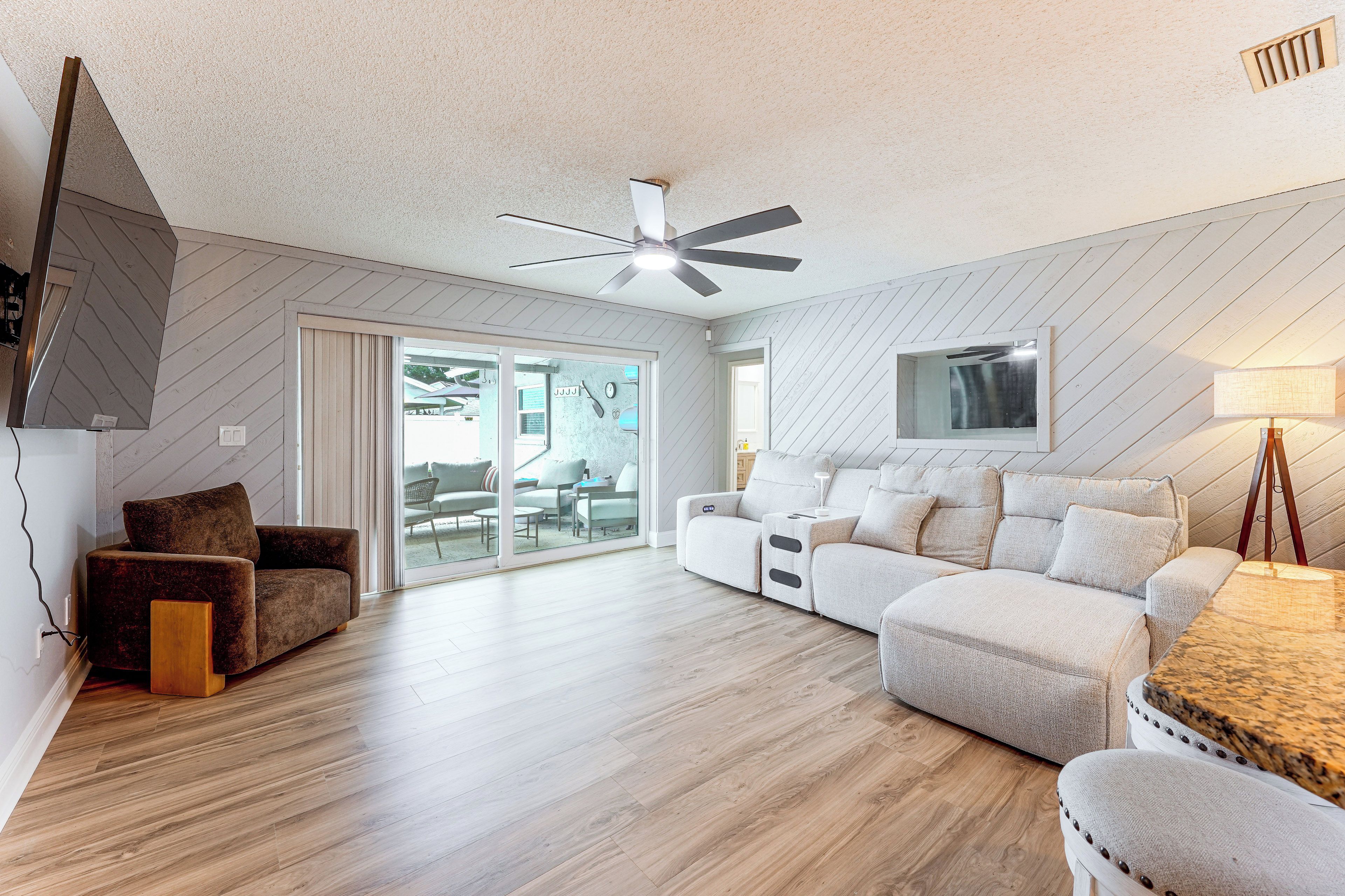 A modern living room with a ceiling fan, a flat-screen TV mounted on the wall, and a sectional sofa.