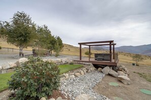 Ein rustikaler Außenbereich mit Holzpergola, Grill und Blick auf eine hügelige Landschaft.