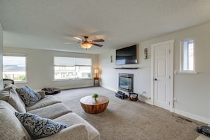 A living room with a ceiling fan, a flat-screen TV mounted above a fireplace, a sofa with patterned cushions, and a round coffee table with a plant. - Seasonal Private Pool: Tacoma Home w/ Patio & BBQ! (Tacoma)