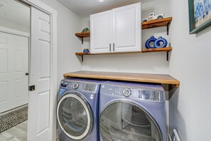 A laundry room with a front-loading washer and dryer, wooden shelves above, and a white door to the left. - Seasonal Private Pool: Tacoma Home w/ Patio & BBQ! (Tacoma)