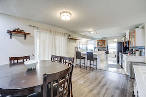 A dining area with a wooden table and chairs, a kitchen with white cabinets, and a small island with bar stools. - Seasonal Private Pool: Tacoma Home w/ Patio & BBQ! (Tacoma)