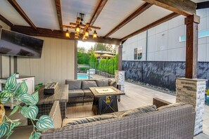 An outdoor patio with a sofa, table, and TV screen, overlooking a swimming pool and garden. - Seasonal Private Pool: Tacoma Home w/ Patio & BBQ! (Tacoma)