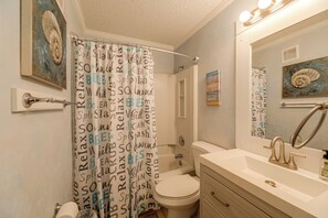 Ein Badezimmer mit Duschvorhang mit motivierenden Sprüchen, Toilette, Waschbecken mit Spiegel und einer Wandleuchte.