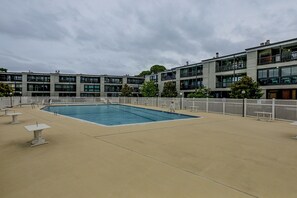 Área de piscina com piscina, espreguiçadeiras e cerca branca.