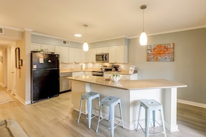 Cozinha moderna com ilha central, banquetas e micro-ondas.