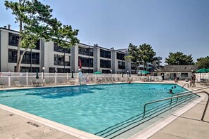 Ein Swimmingpool mit weißem Zaun, Liegestühlen und Sonnenschirmen.