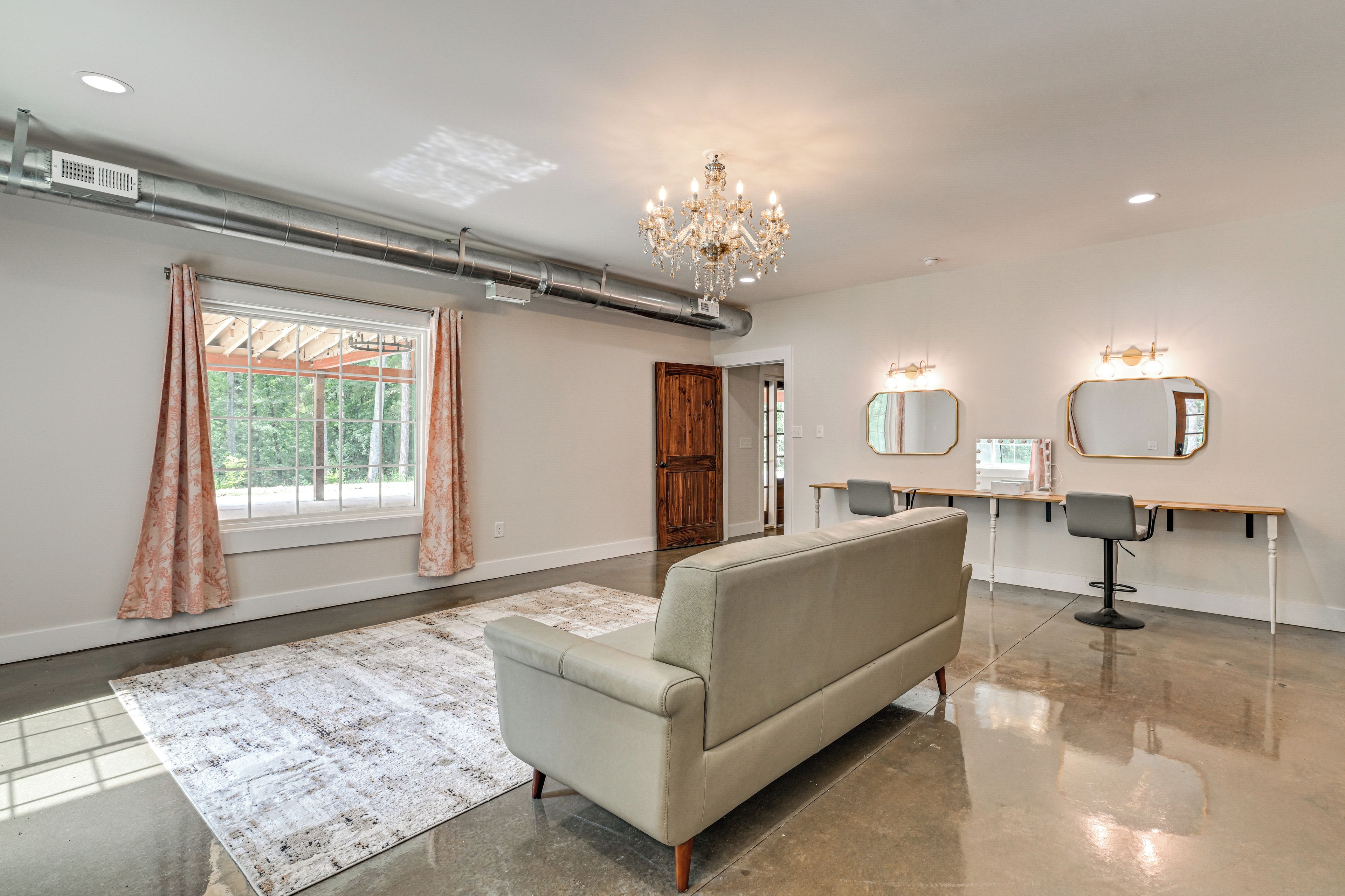 Un salon moderne avec un canapé, un lustre, une grande fenêtre avec des rideaux et une coiffeuse avec des miroirs.