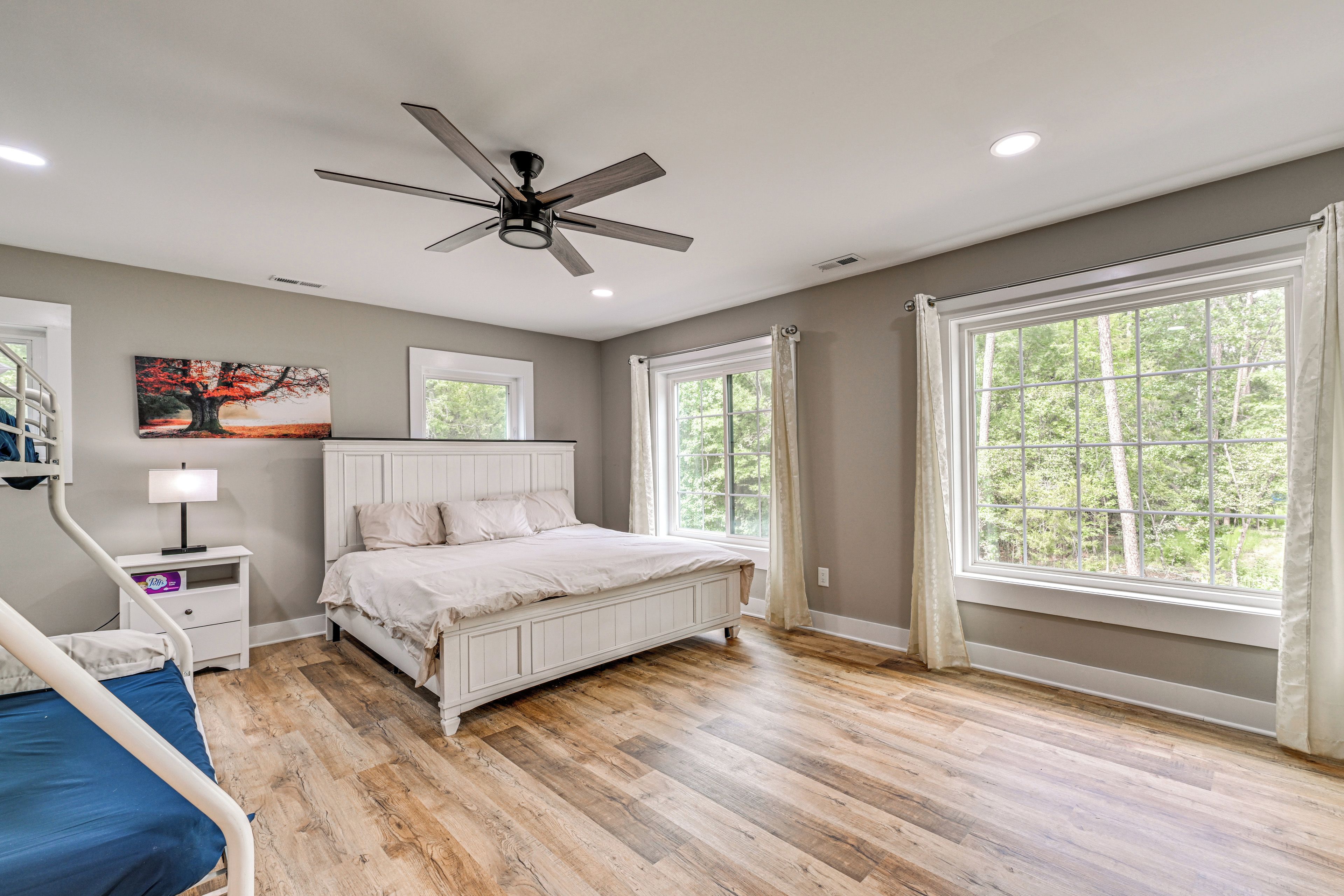 A bedroom with a bed, a ceiling fan, a window, and a painting on the wall.