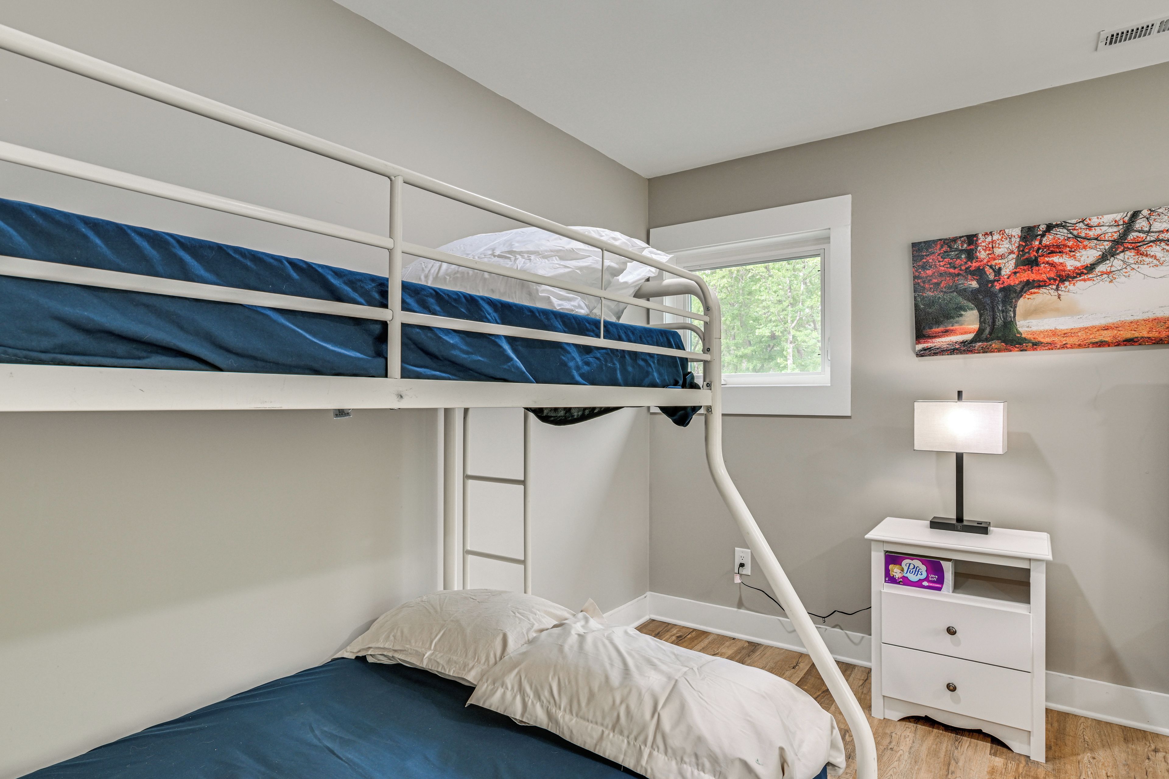 Un lit superposé avec une fenêtre, une table de chevet avec une lampe et un tableau accroché au mur.