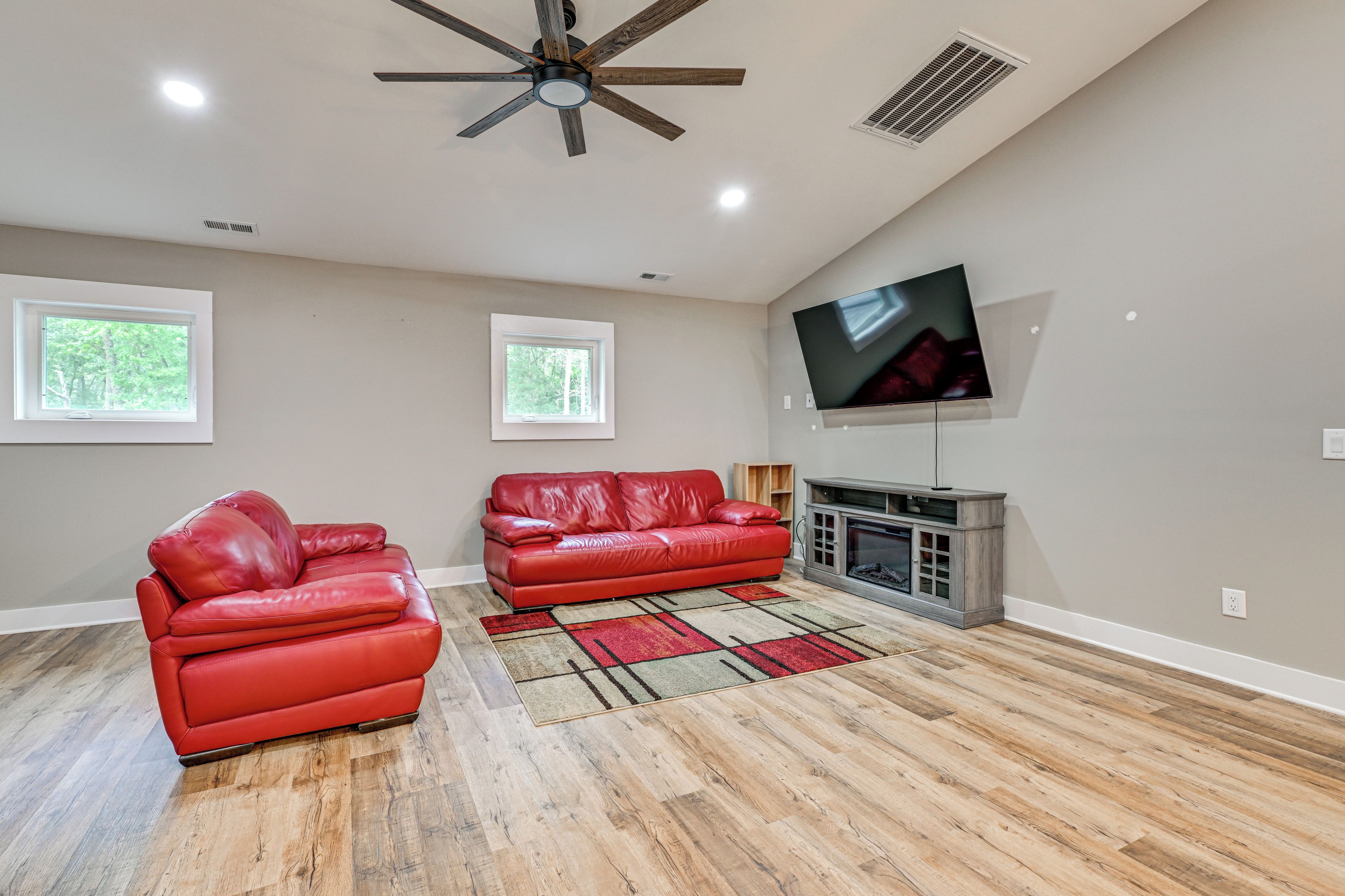 Un salon spacieux avec une cheminée, deux canapés en cuir rouge, un grand téléviseur à écran plat et un plancher en bois.