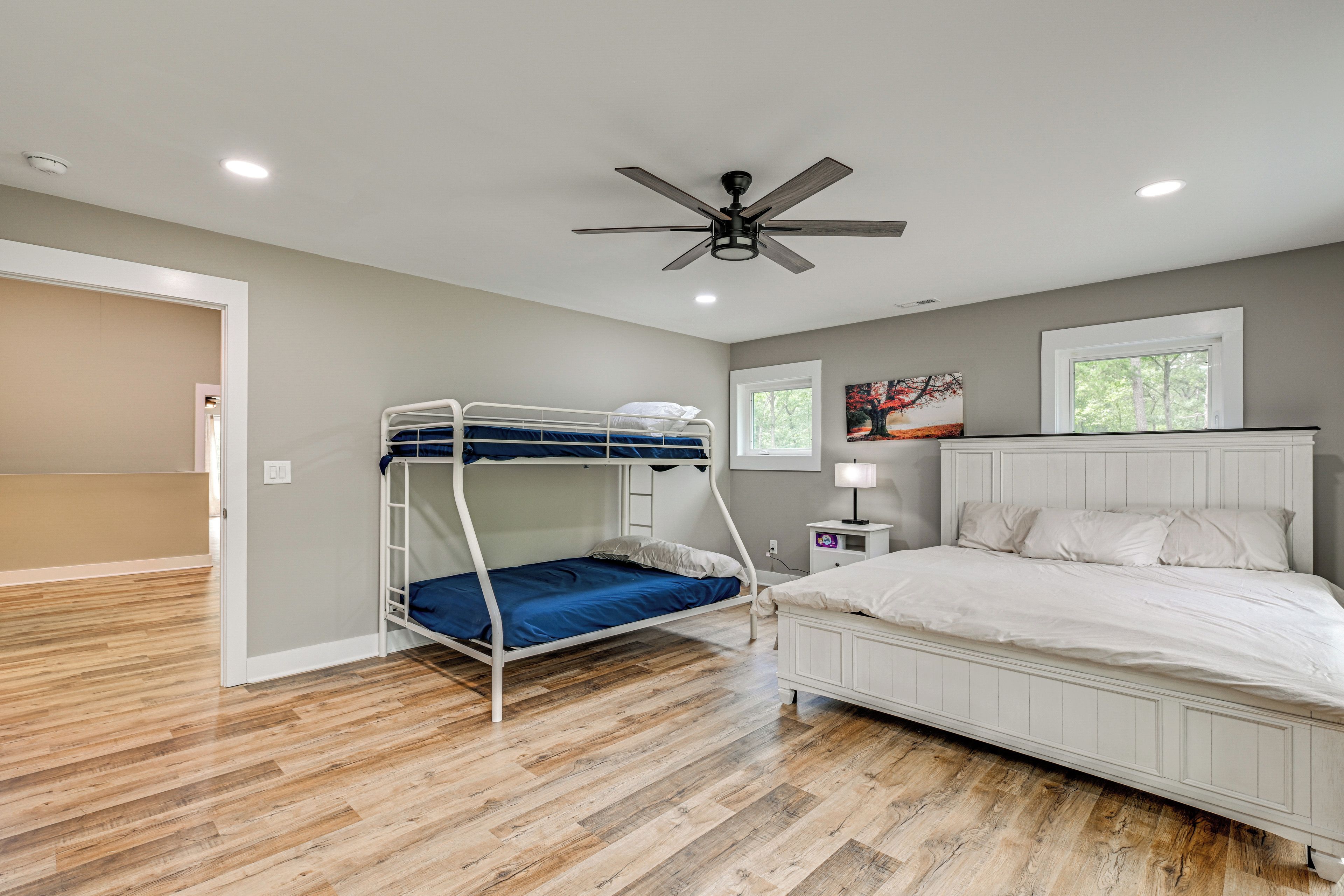 Une chambre avec un lit superposé, un lit simple, un ventilateur de plafond et une fenêtre donnant sur les arbres.