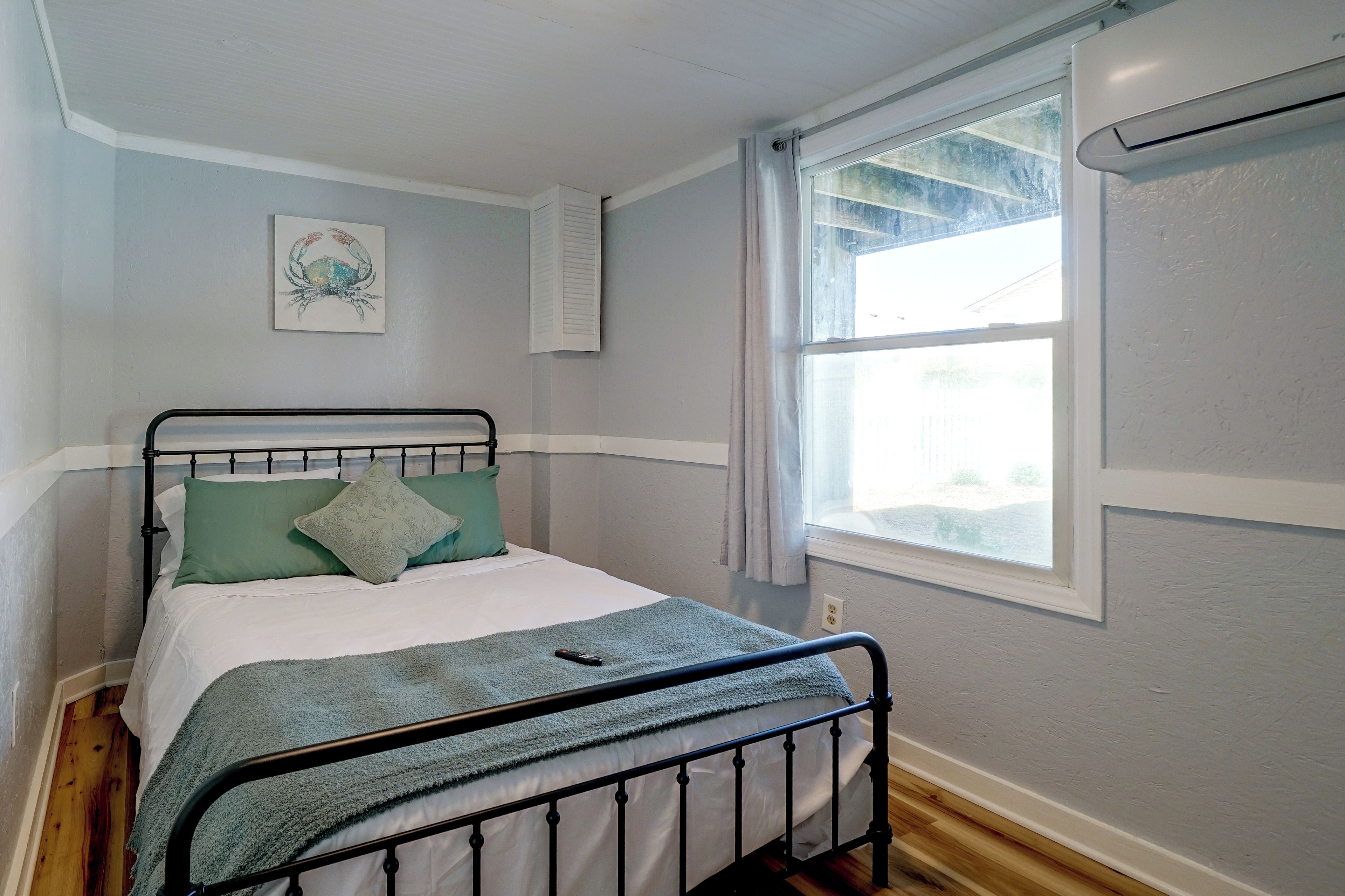 A bedroom with a bed, a window, a wall-mounted air conditioner, and a painting.