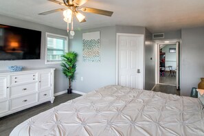 A bedroom with a large bed, a dresser, a ceiling fan, a window with blinds, a plant, and a door leading to another room. - Game Room & Hot Tub! Bayfront Family Gem (Fort Walton Beach)