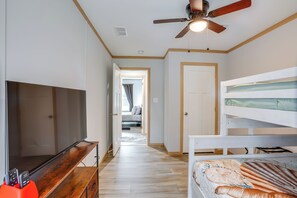 Een slaapkamer met een bed, een televisie, een plafondventilator en een gang naar een andere kamer.