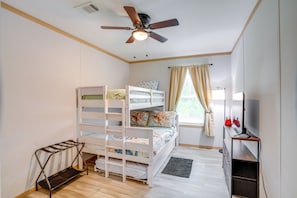 Ein Zimmer mit Etagenbetten, einem Deckenventilator, einem Schreibtisch mit Stuhl, einem Fenster mit Vorhängen und einem kleinen Teppich.