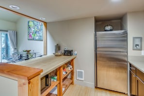 A modern kitchen with a wooden countertop, stainless steel refrigerator, and a dining area with a glass table and chairs. - Walk to Ski Slopes! Sun Valley Condo w/ Balcony (Ketchum)