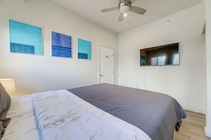 A bedroom with a bed, a ceiling fan, a door, and three wall-mounted paintings. - Sun, Surf & Pier Views: Santa Monica Beach Condo! (Santa Monica)