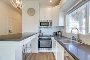 A modern kitchen with stainless steel appliances, white cabinetry, and a large window providing natural light. - Sun, Surf & Pier Views: Santa Monica Beach Condo! (Santa Monica)