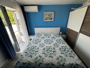 A bedroom with a bed, a nightstand, a wall-mounted air conditioner, a window with curtains, and a framed picture on the wall. - Petra With Private Pool (Rab)