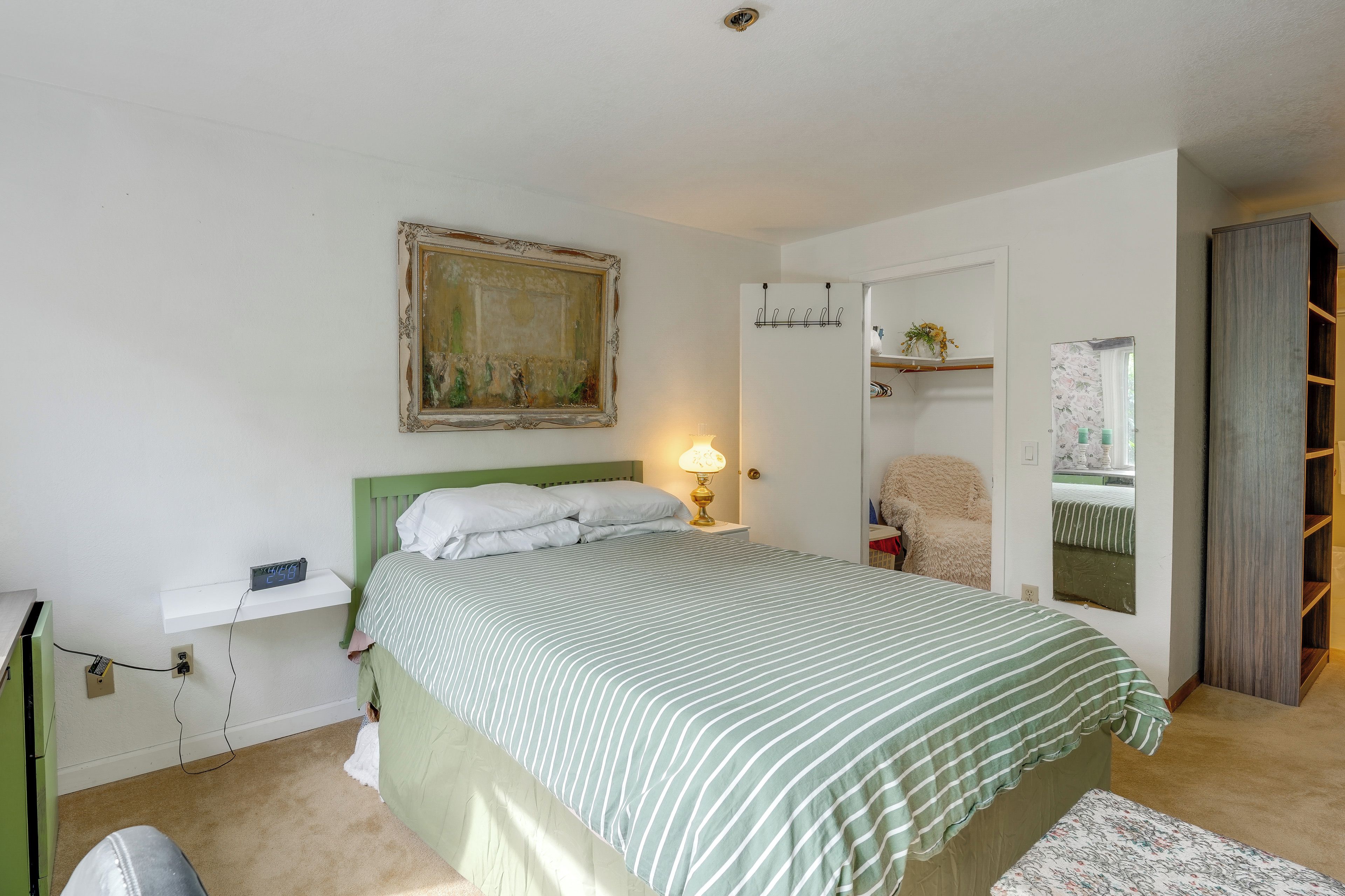 A bedroom with a bed, a bedside table with a lamp, a painting on the wall, and a wardrobe.