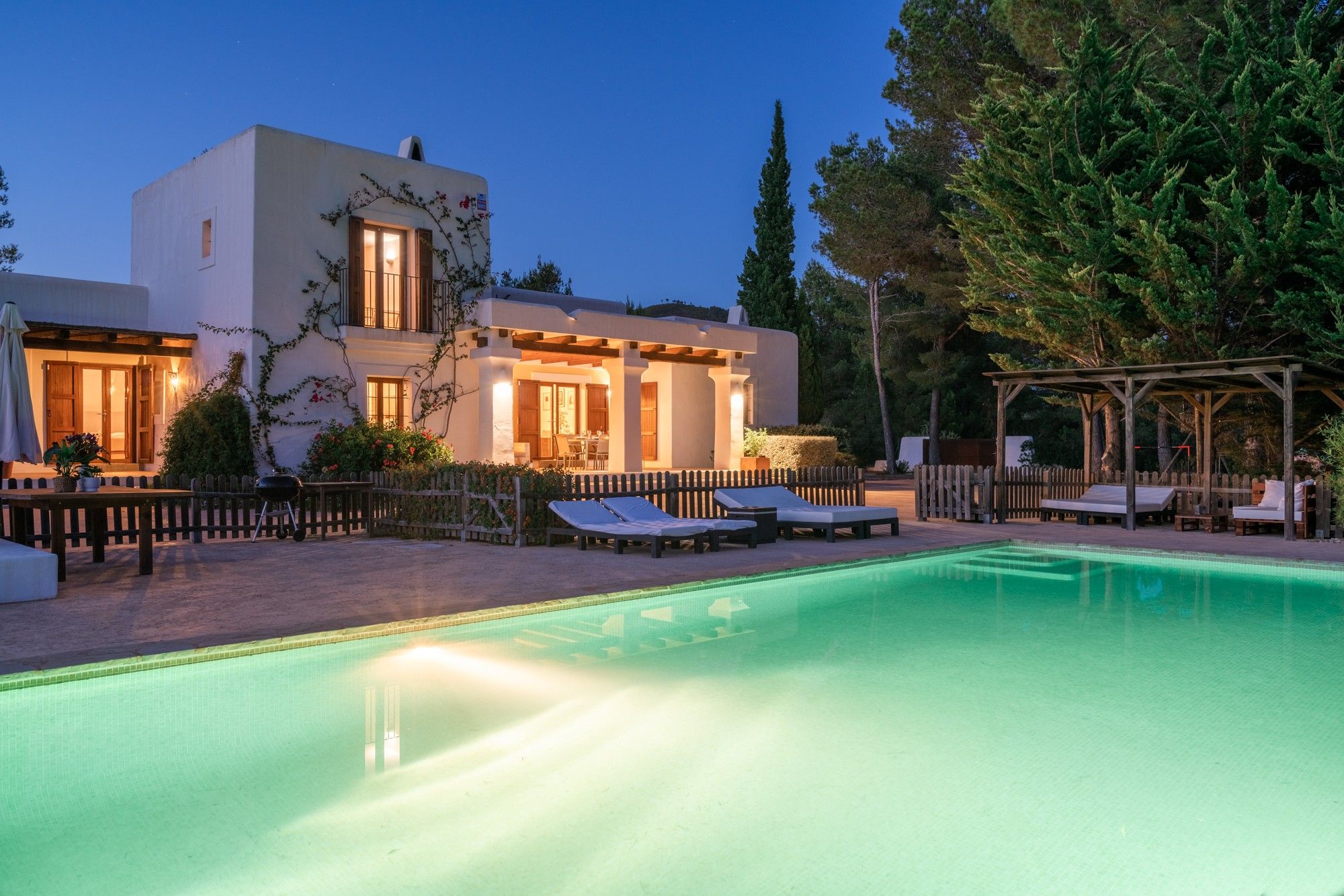 Una villa moderna con piscina, mobiliario exterior y una pérgola de madera.