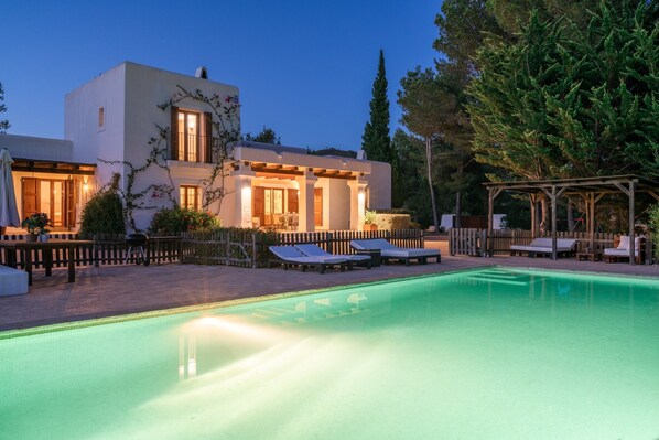 A modern villa with a swimming pool, outdoor seating, and a wooden pergola.