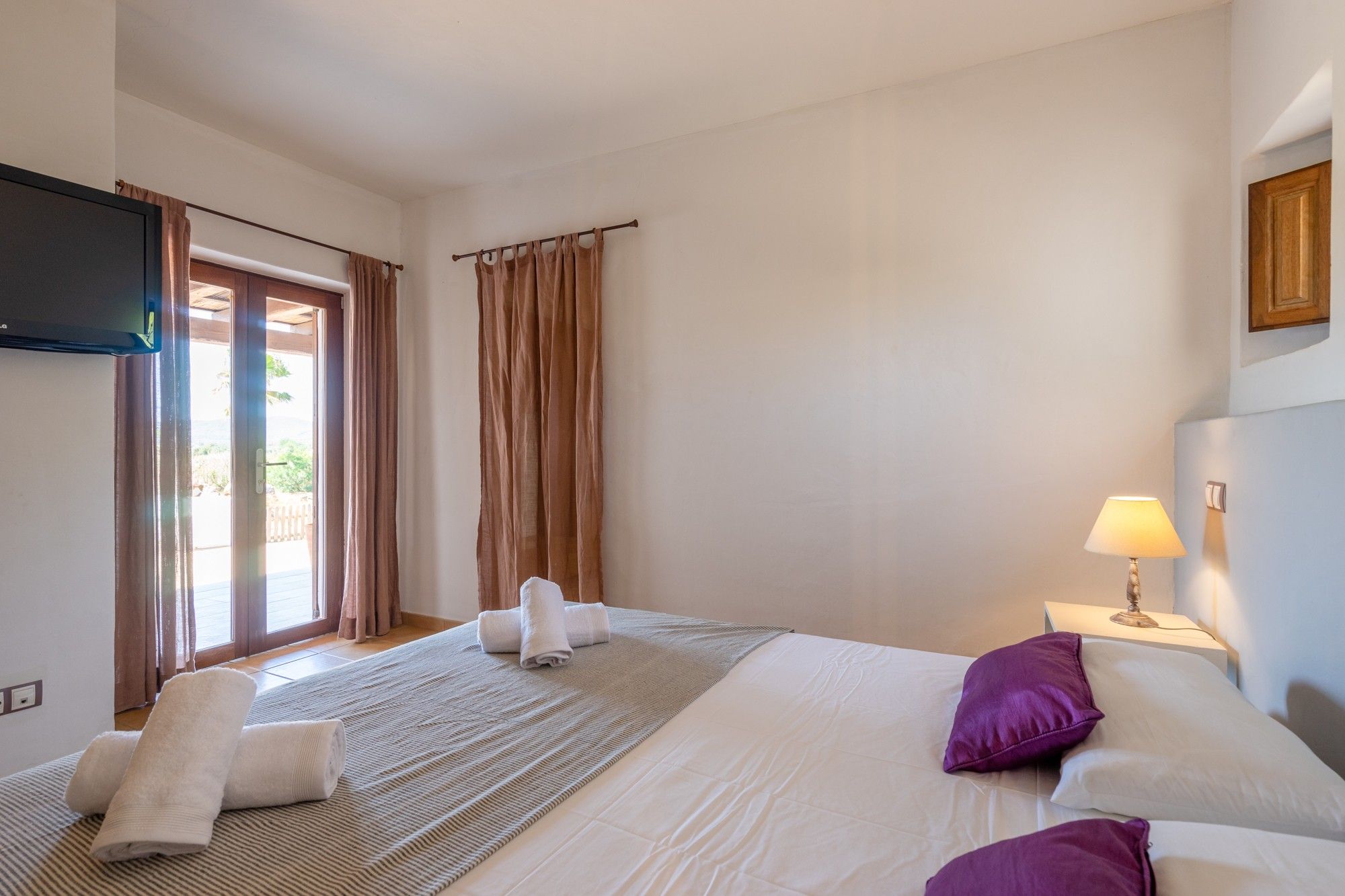 Camera d'albergo con un letto, una TV a schermo piatto, una lampada da comodino e vista sull'esterno tramite una porta.