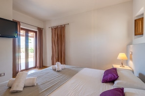 A hotel room with a bed, a flat-screen TV, a bedside lamp, and a view of the outdoors through a door.