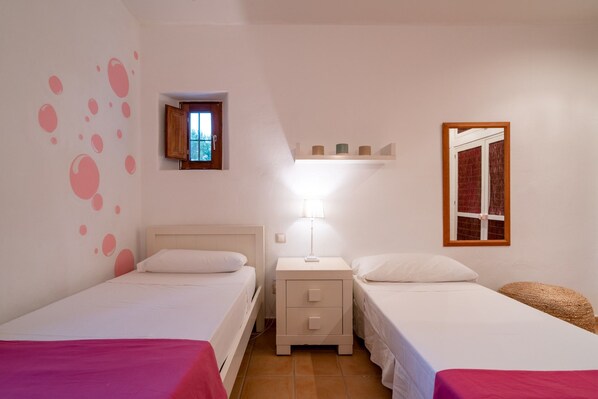 Una stanza con due letti, un comodino con lampada, una piccola finestra e uno scaffale sopra il letto.