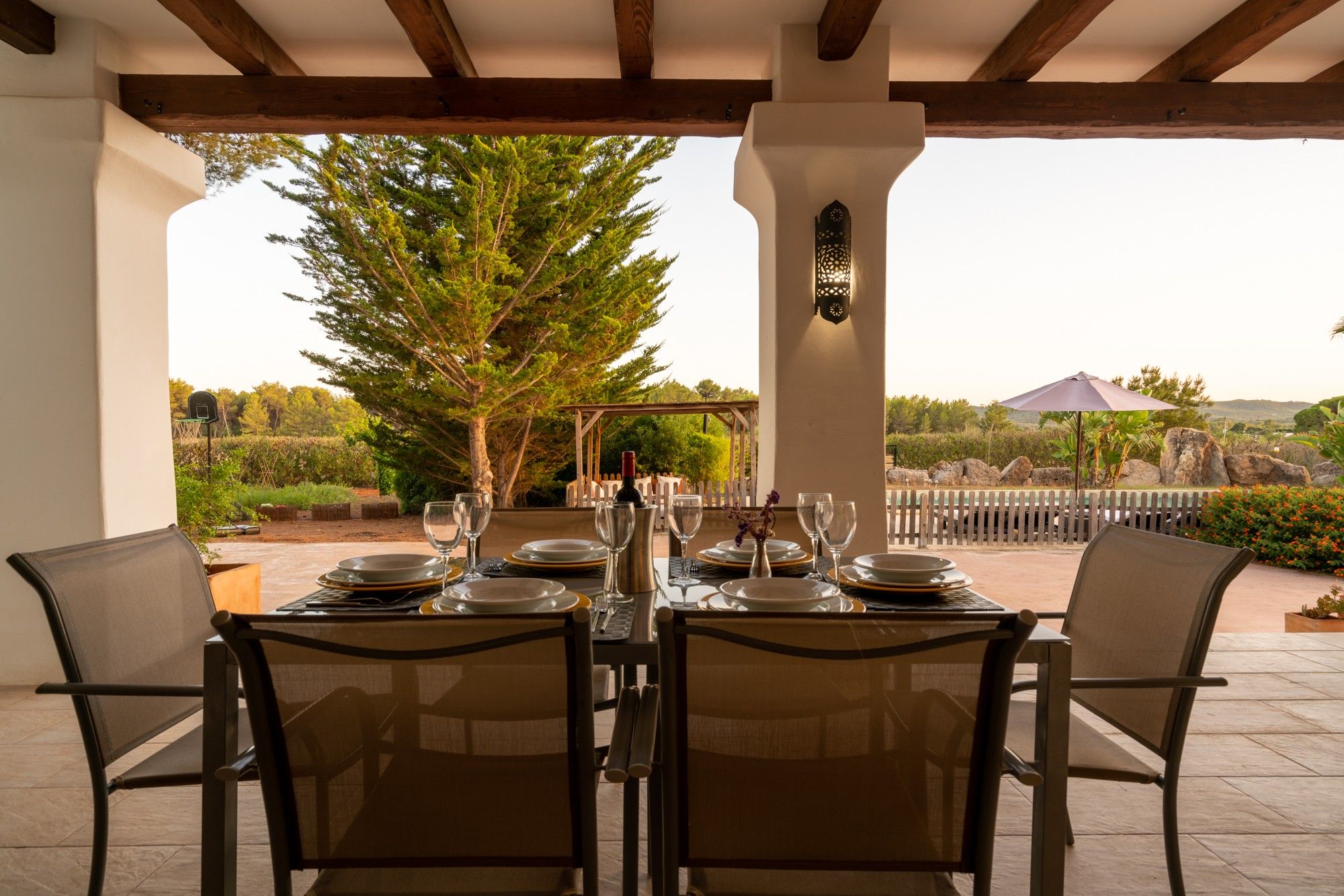 An outdoor dining area with a table set for four, surrounded by chairs, and a pergola overhead.