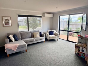 Una sala de estar con un sofá gris, un sillón blanco y un ventanal con vista a un jardín.