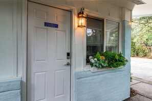 A white door with a blue sign, a window with a light fixture, and a planter with green plants. - Hot Tub & Dock Access! Bayfront Studio (Fort Walton Beach)