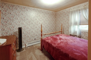Une chambre avec un papier peint à motifs floraux, un lit en bois, une commode et un radiateur.