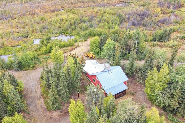 A red building with a blue roof surrounded by dense forest and a small pond.