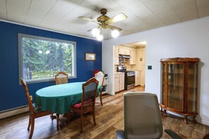 A dining area with a table, chairs, a ceiling fan, and a view through a window.