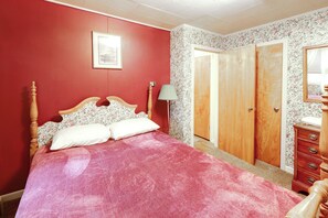 A bedroom with a wooden bed, a red wall, a floral wallpaper, a door, and a dresser.