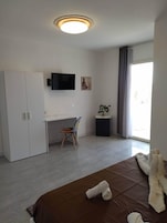 Un dormitorio con cama, escritorio, silla, televisor y ventana con cortinas.