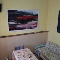 Una habitación con un cuadro abstracto grande en la pared, una mesa con mantel floral, dos sillas y un sofá.