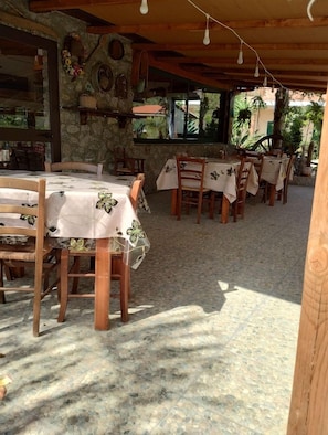 Un área de comedor al aire libre con paredes de piedra, mesas y sillas de madera.