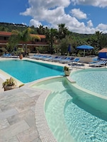 Un área de piscina con dos piscinas rectangulares, sillas de descanso y sombrillas.