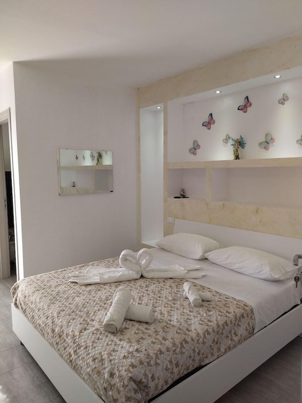 A modern bedroom with a large bed, a bedside mirror, and butterfly wall decor. - Residence Heaven (Ricadi)