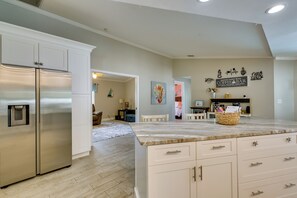 A kitchen with a stainless steel refrigerator, white cabinetry, and a marble countertop. - Saltwater Pool & Firepits: Cape Coral Home (Cape Coral)