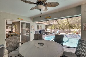 A poolside area with a table and chairs, a ceiling fan, and a view of a swimming pool. - Saltwater Pool & Firepits: Cape Coral Home (Cape Coral)