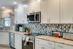 A modern kitchen with white cabinetry, a microwave, a stove, and a toaster. - Saltwater Pool & Firepits: Cape Coral Home (Cape Coral)