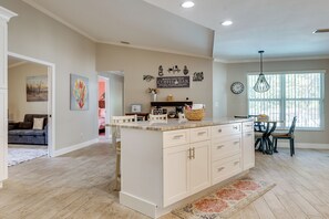A spacious kitchen with a central island, a dining area with a table and chairs, and a living room with a sofa and artwork. - Saltwater Pool & Firepits: Cape Coral Home (Cape Coral)