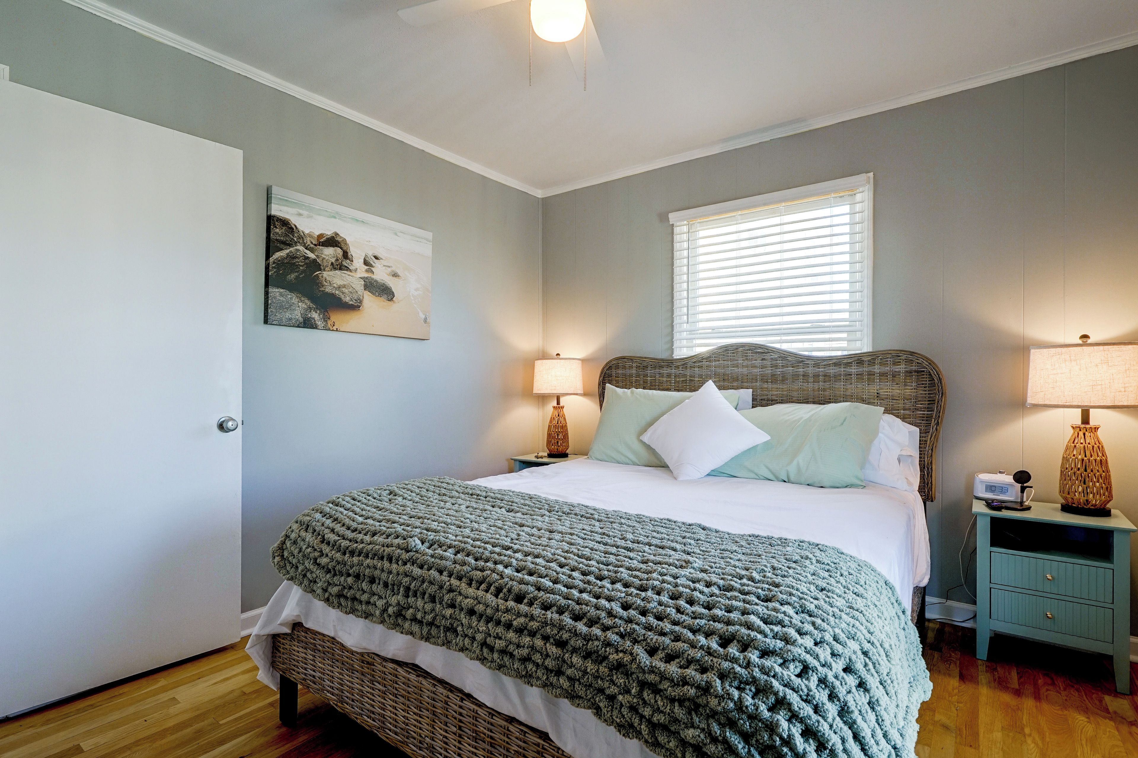 Un dormitorio con cama, lámparas de noche, un cuadro en la pared y una ventana con persianas.