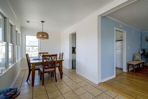 A spacious dining area with a wooden table and chairs, a hanging light fixture, and a view through an open doorway to a kitchen area. - Salty Chateau Home w/ Ocean Views, Surf City (Surf City)